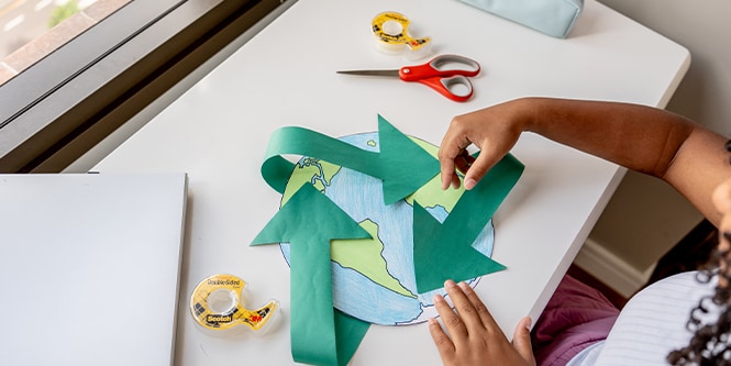Mädchen bastelt eine Weltkarte aus Papier mit Materialien der Marke Scotch™

