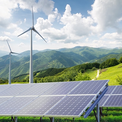 Eine Berglandschaft mit Windrädern und Solarzellenplatten im Vordergrund.