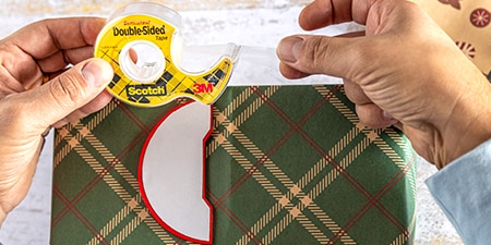 Dekorationen an einem verpackten Geschenk mit Scotch® doppelseitigem Klebeband befestigen
