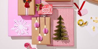 Weihnachtsdekorationen und Papierbasteleien wie Bäume und Kugeln mit Scotch® doppelseitigem Klebeband an verpackten Geschenken befestigen
