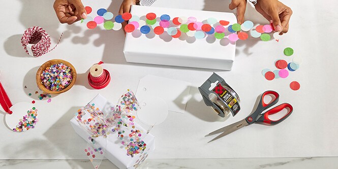 Frau und ihre Tochter verpacken eine Geschenkbox mit Konfettiklebeband, hergestellt durch das Ankleben von buntem Konfetti auf Scotch® Verpackungsklebeband
