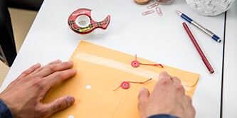Mann beim Verschließen eines Umschlags mit Scotch® Super-Hold Tape
